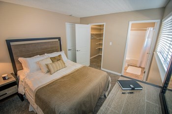 Bedroom with large closet and custom shelving to left and bathroom to right. Staged with bed and dresser. - Photo Gallery 9