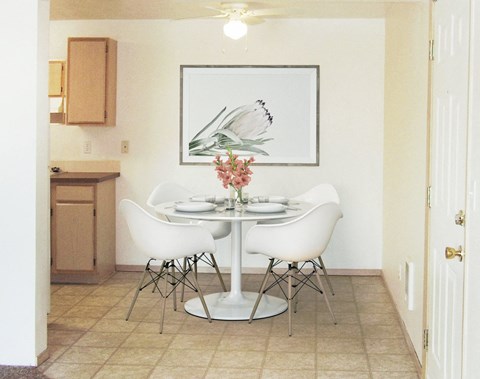 Dining area with ceiling fan, and the kitchen to the left. Staged with a table, 4 chairs, wall art, and flowers.at North Pointe, Post Falls Idaho
