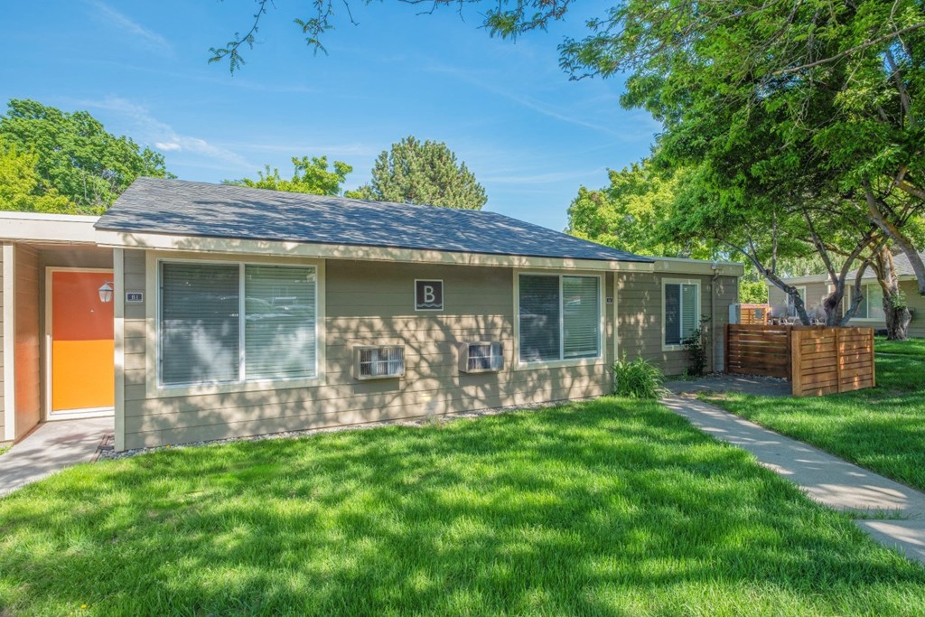 A Park View apartment home with an orange door and a yard with green grass, trees and a private patio.at Park View Apartments, Wenatchee, WA