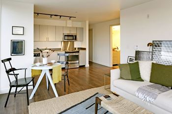 Open living area that looks into the dining room and kitchen. Staged with a couch, table, chairs, and a dining set.at 19th & Mercer, Seattle, 98112