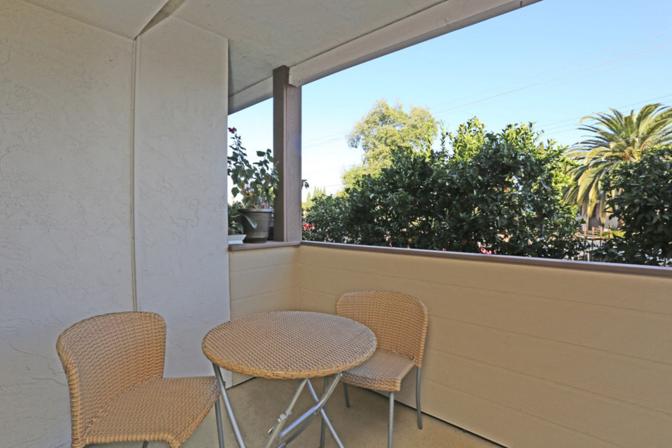 Apartment private patio with small table and two chairs overlooking trees on a sunny day at Pacific Sands, California, 92117