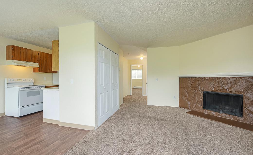 Spacious carpeted living room divided by wall with double door closet opposite a fireplace and mantle.