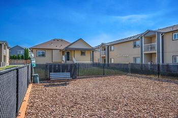 Fenced in dog park with bench and bag dispensing station. Surrounded by green grass and apartments.at Pine Tree Park, Washington, 99337