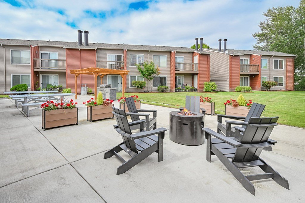 A patio with chairs and a fire pit in front of apartment buildings.