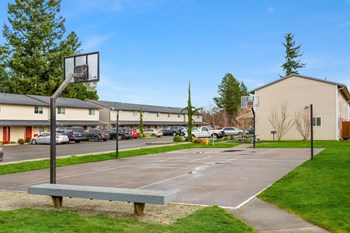 Outdoor basketball court with two hoops opposite each other, surrounded by grass, a bench, a picnic table, and trees. - Photo Gallery 17