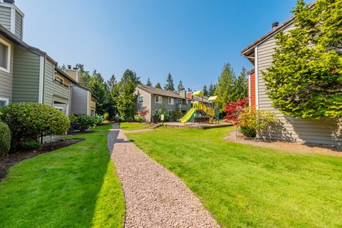 A playground with a slide is in the middle of a grassy area between two rows of houses.