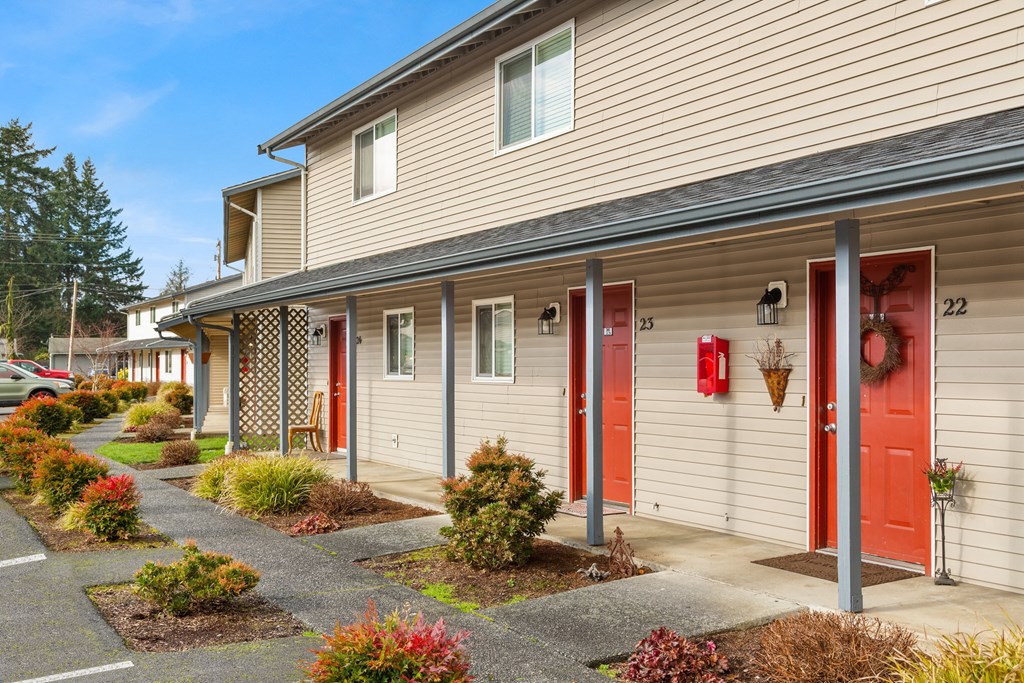 Outside apartments with red doors and paved walkways with colorful landscaping leading to each door.at Quilceda Gardens, Marysville, WA