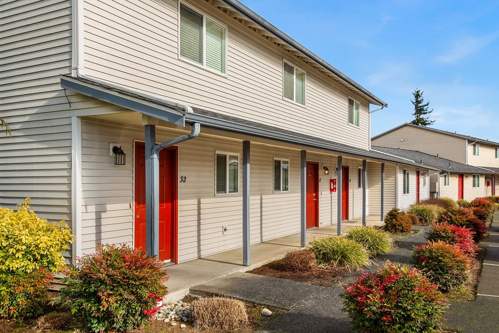 Apartment building exterior with a paved walkway lined with flowers and bushes.at Quilceda Gardens, Marysville, 98270