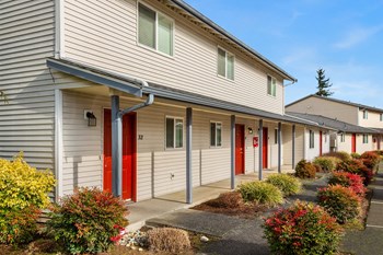 Community Exterior Apartment building exterior with a paved walkway lined with flowers and bushes. - Photo Gallery 5