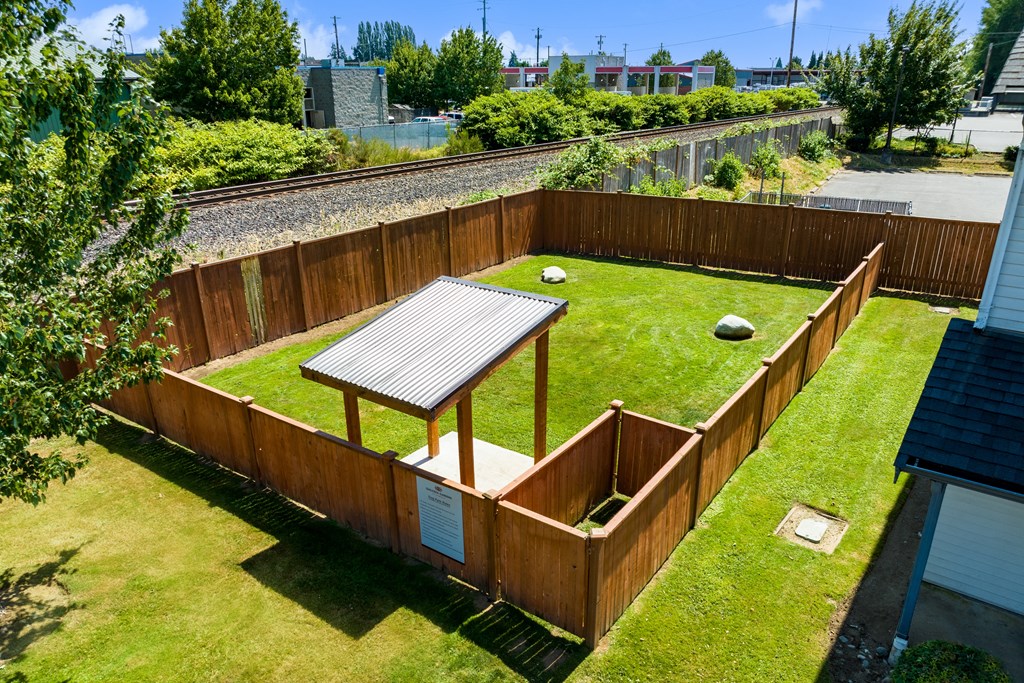 a dog park with large grassy area, covered section for shade and rain protection and rocks