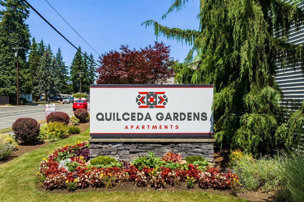 a sign for Quilceda Gardens Apartments in front of trees and flowers