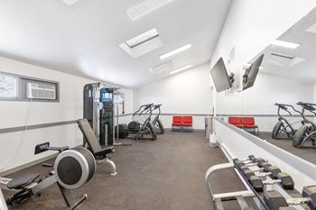 A gym with a variety of equipment including a rowing machine, dumbbells, and a bench.