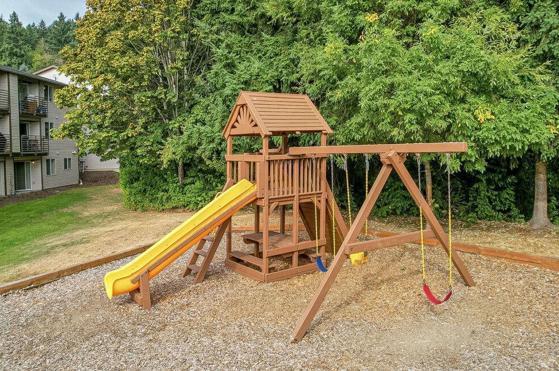 a wooden swing set with a yellow slide in a backyard