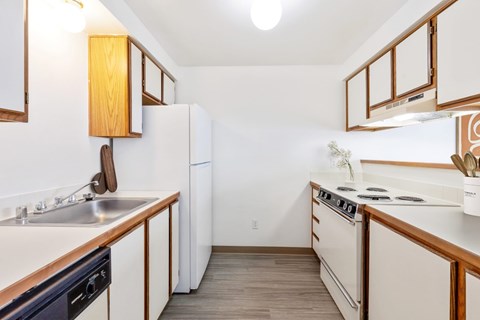 A double galley kitchen with white appliances and wooden cabinets at Shiloh Glen Apartments in Bilings.