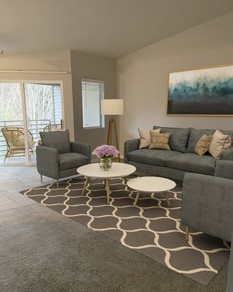 Living room with large sliding glass doors to private covered patio. Staged with 2 chairs, a couch, coffee tables, lamp.at Sitka Heights, Fife Washington