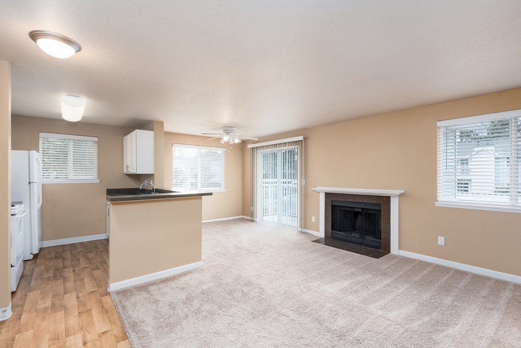 an empty living room with a fireplace and a kitchen