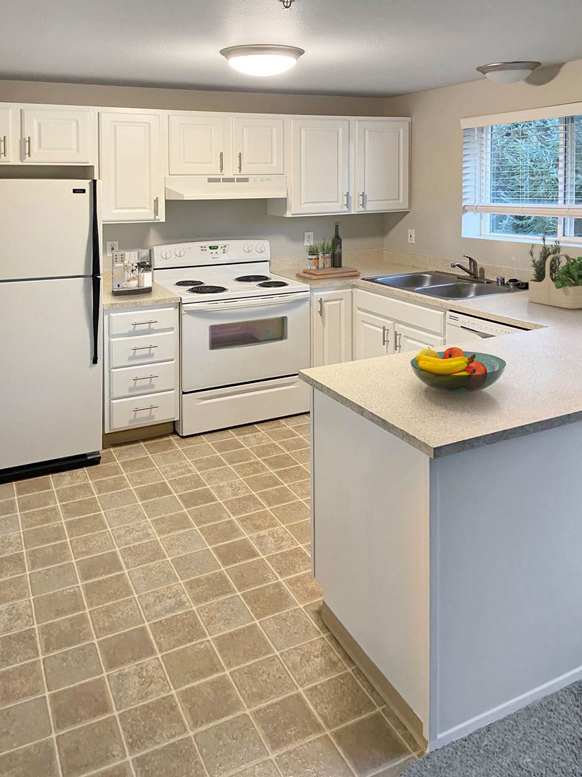 Kitchen U-shaped kitchen with full-size fridge, stovetop and oven, sink with garbage disposal, dishwasher, and white cabinets.at Sitka Heights, Fife