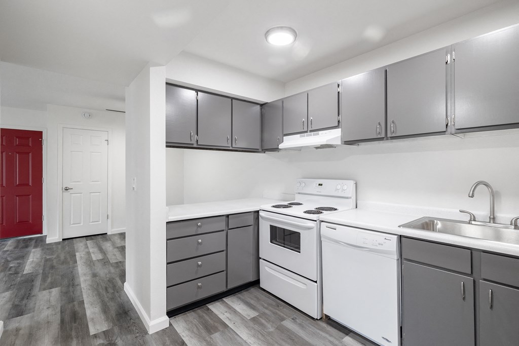 an open kitchen at Summit Apartments with grey cabinets and faux wood flooring, white countertop and white appliances.