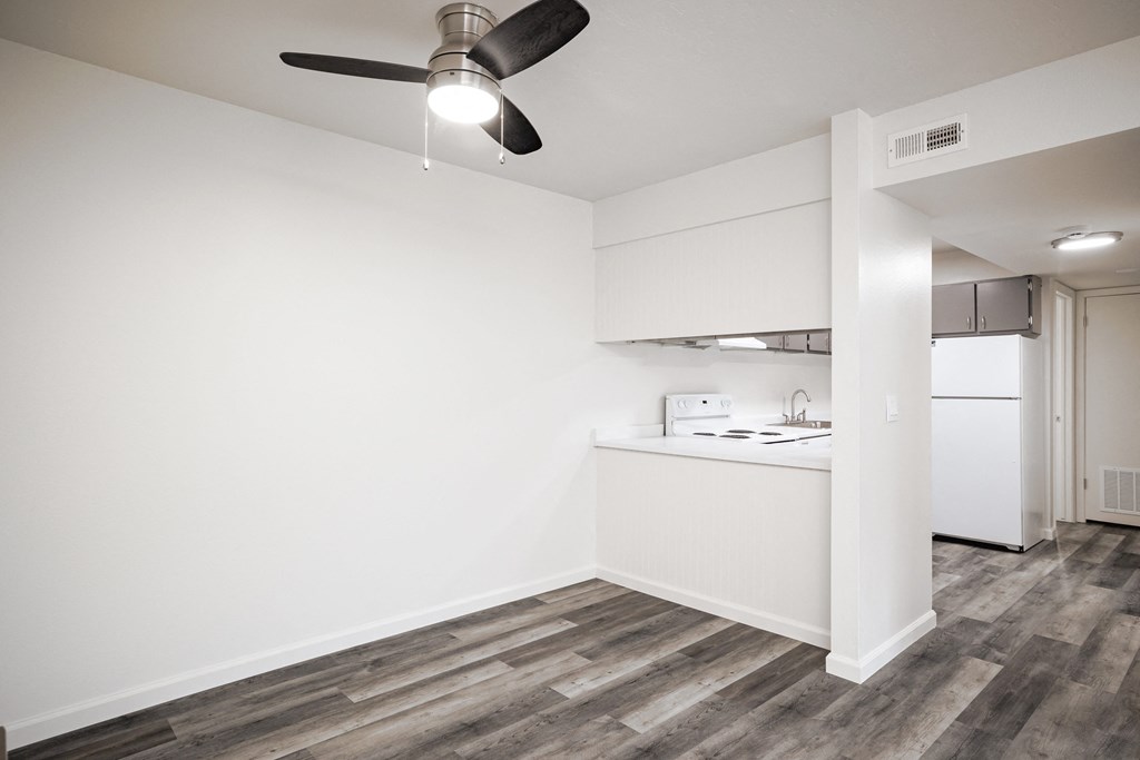 an empty living room with a kitchen and a ceiling fan