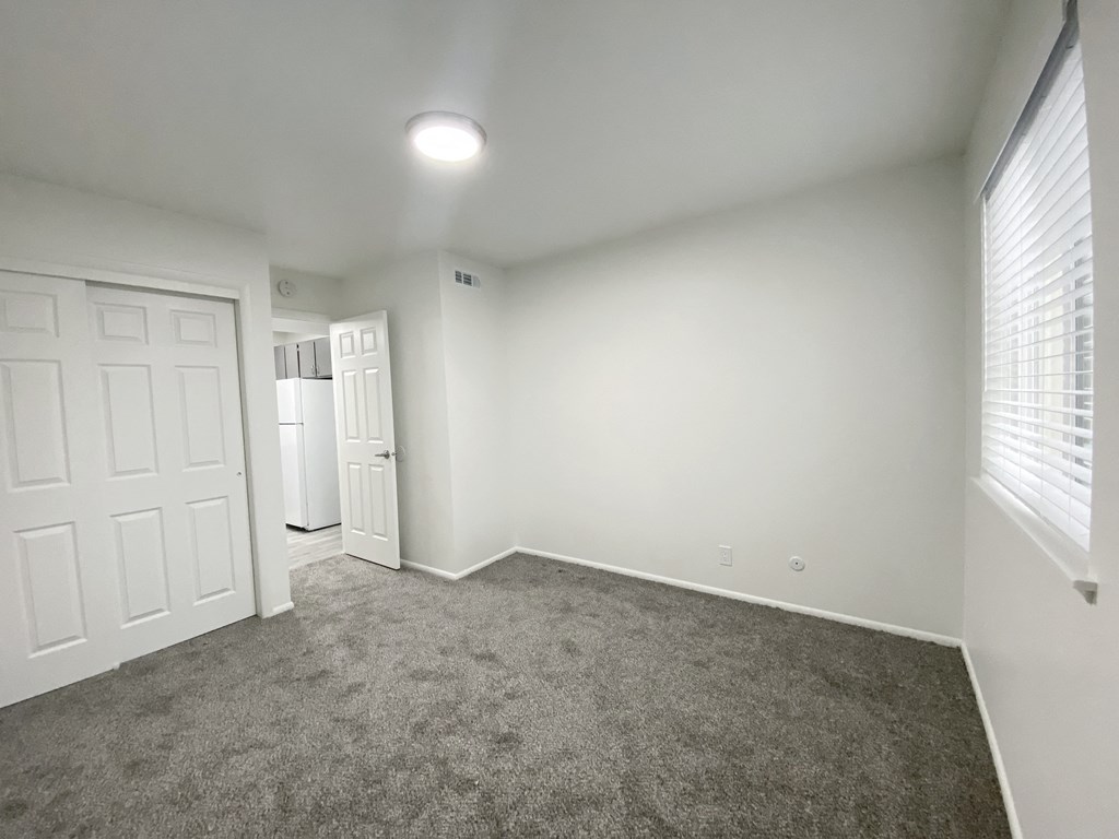 Bedroom with large sliding door closet, oversized window with white blinds on right, and door to hallway in back left corner at Summit, Pocatello, ID 83201