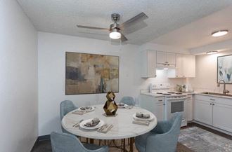 Dining room with wood-like flooring and a ceiling fan opens into spacious kitchen. Staged with a round table, 4 blue chairs and art. at Talavera, Boise, 83705