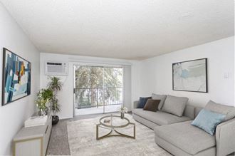 a spacious living room white walls, taupe carpet, and huge double sliding glass doors to private balcony. Staged with a gray couch, a coffee table, console table and wall art. at Talavera, Idaho