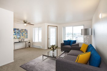 Living room with ceiling fan light and access to private balcony. Staged with couch, accent chair, coffee table, lamp, art. - Photo Gallery 9