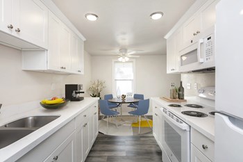 Kitchen looks into the dining area with a window behind. Staged with a coffee machine, dining set, and house plant. - Photo Gallery 11