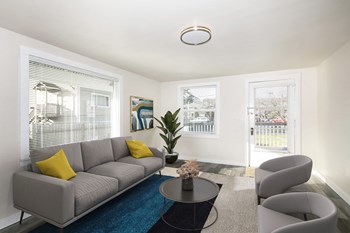 Living room with two large windows and a door to private balcony. Staged with a couch, coffee table, two chairs, plant, rug. - Photo Gallery 12