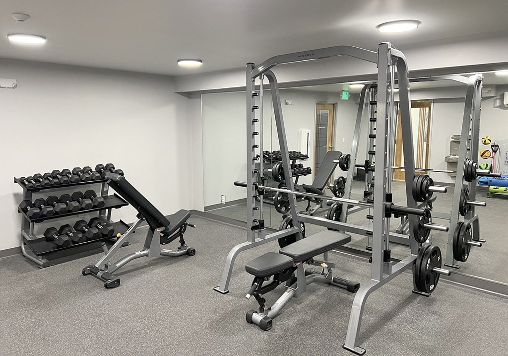 Fitness center with weight rack, free weights, squat, bench press rack, and two benches at University Glen, University Place, Washington