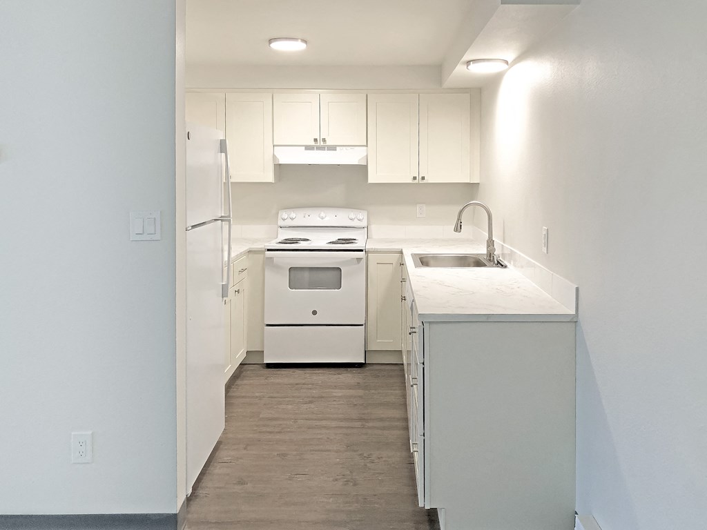 Updated kitchen with white top and bottom cabinets, full-size fridge, oven, stovetop, rangehood, sink, and dishwasher at Talavera, Boise, 83705.