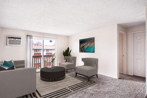 Living room with white walls, taupe carpet, and sliding glass doors to a private balcony. Staged with a gray couch, 2 chairs, a coffee table, and rug.at Wildflower, Kennewick Washington
