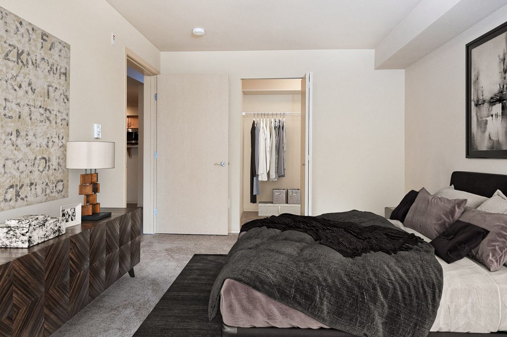 Carpeted bedroom with a queen size bed, a long set of drawers, art on the walls, and a closet with an accordion door at 6 Wood Flats, Lacey, WA