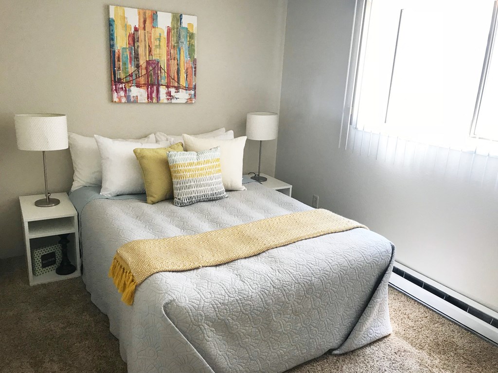 Bedroom with queen sized bed and large window with blinds. Staged with bed, side table, lamp and wall art.at The Lakes Apartments, Moses Lake, 98837