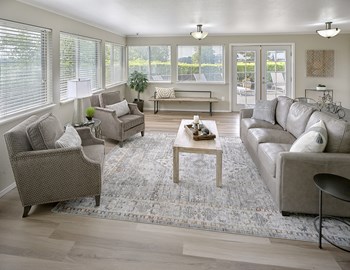 Clubhouse with many windows, a large area rug, a bench, two armchairs, and a couch with a coffee table in the middle. - Photo Gallery 8