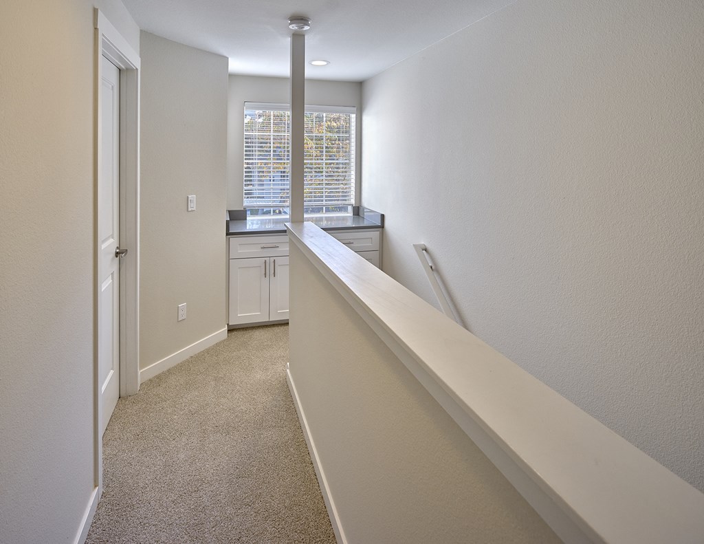 Upstairs carpeted hallway, banister to the right with large window at the top of stairs with counter and cabinets.at Edmonds Gateway, Edmonds, WA