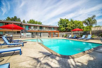 Woodland Village swimming pool surrounded by lawn chairs, umbrellas and blue skies.
