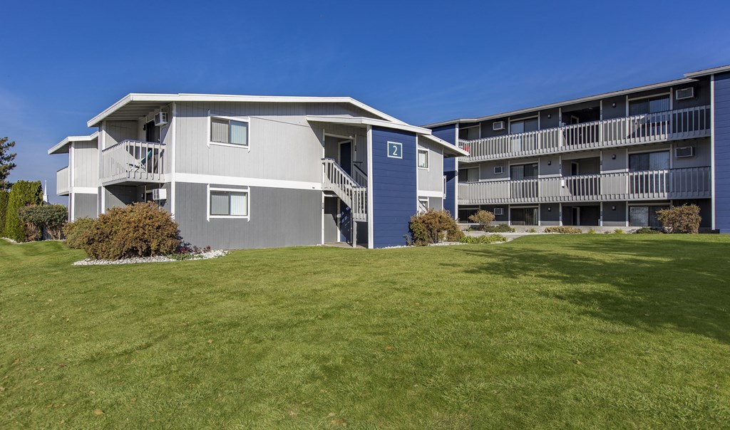 Exterior view of manicured grounds and building, and blue skies in the background at The Lakes Apartments, Moses Lake, WA.