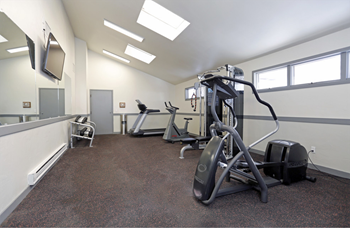Fitness center with an elliptical, cable machine, recumbent bike, treadmill, free weights, a large mirror, and mounted TV. - Photo Gallery 15