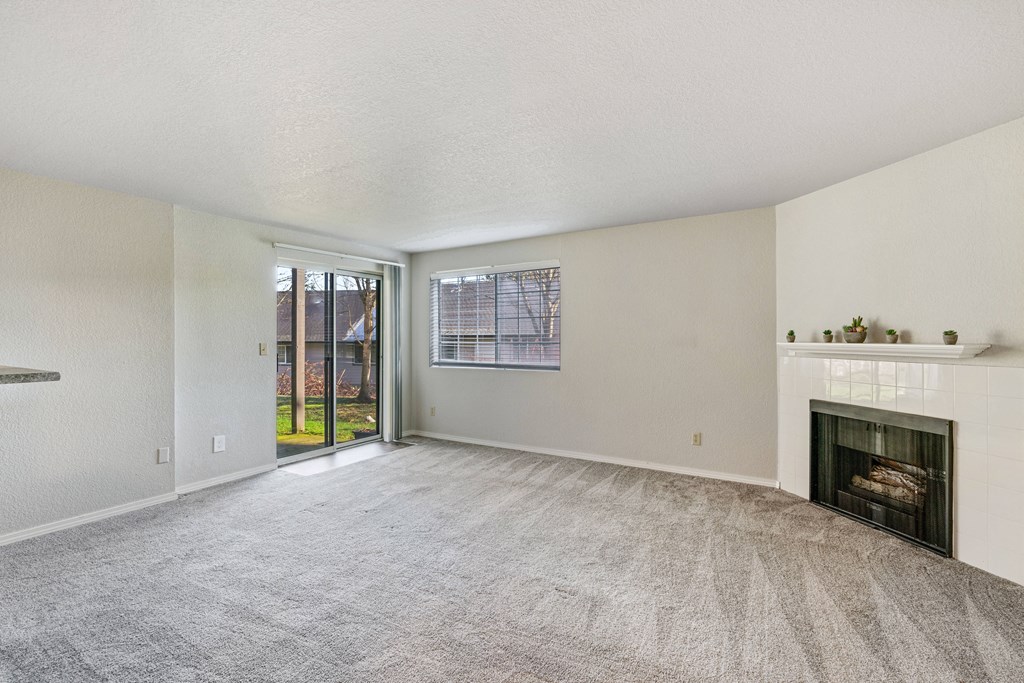 Carpeted living room, gas fireplace, and mantle in the center, with a window and sliding glass doors to a grass lawn.at Capitol Crossing, Olympia, WA