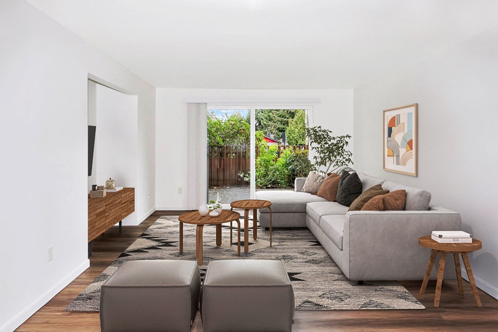 A living room with a grey couch, a wooden coffee table, and a large window with a view of a garden at Heritage Woods Apartments in Renton.