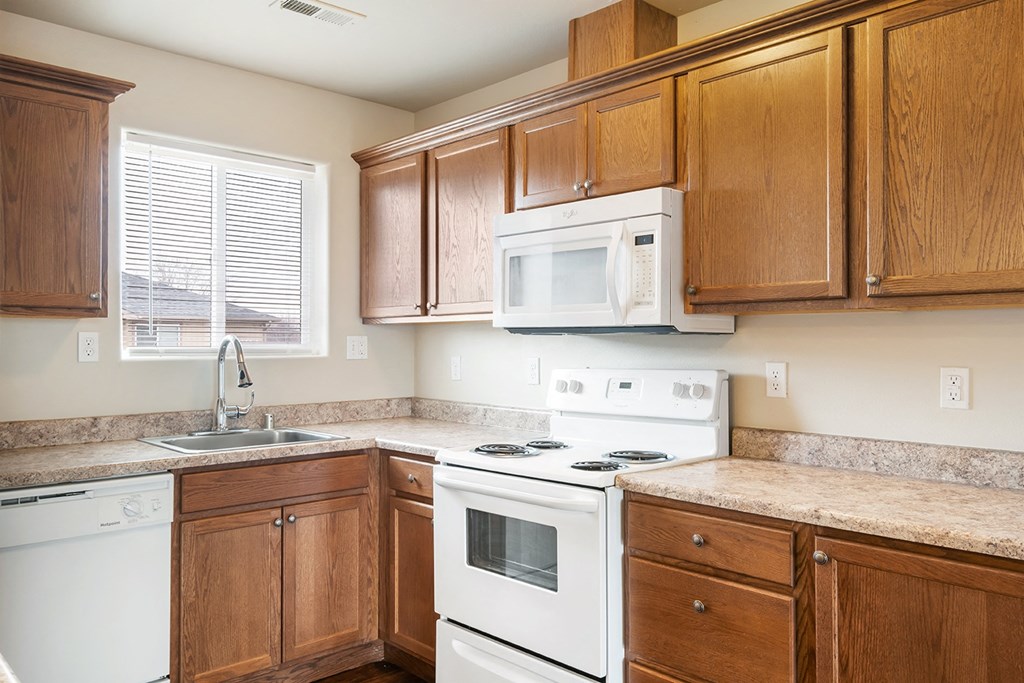 Corner of the kitchen with a dishwasher, sink, oven, and microwave from left to right. Wooden cabinets and a light-filled window on the left wall. at Pine Tree Park, Washington, 99337