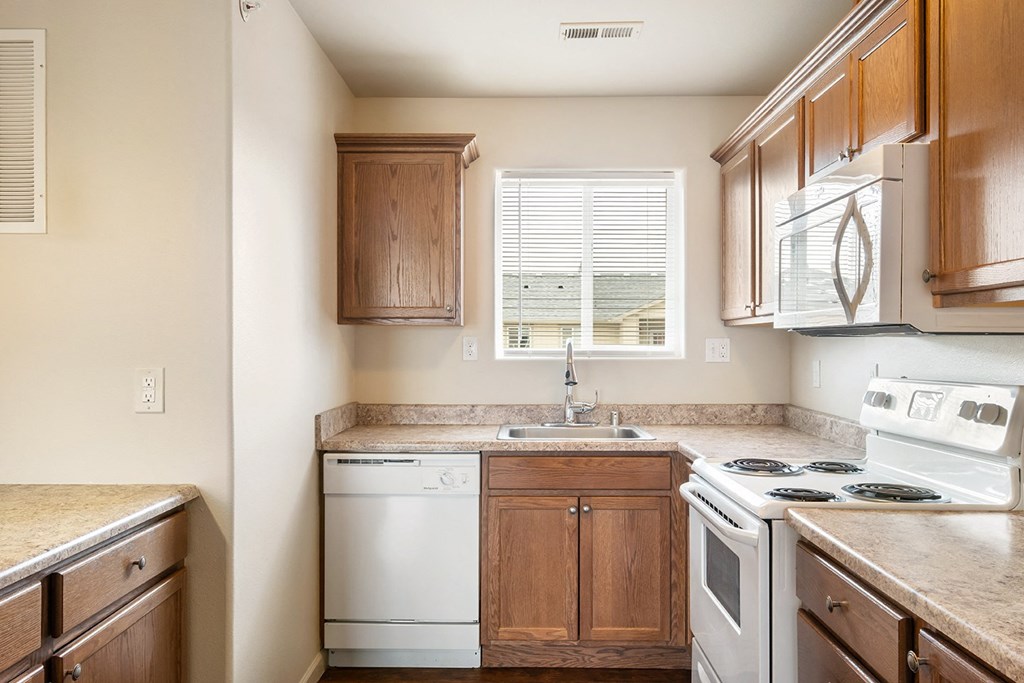 L-shaped kitchen with breakfast bar to the left and white appliances including a dishwasher, stove, oven, microwave, and sink with window above. at Pine Tree Park, Washington