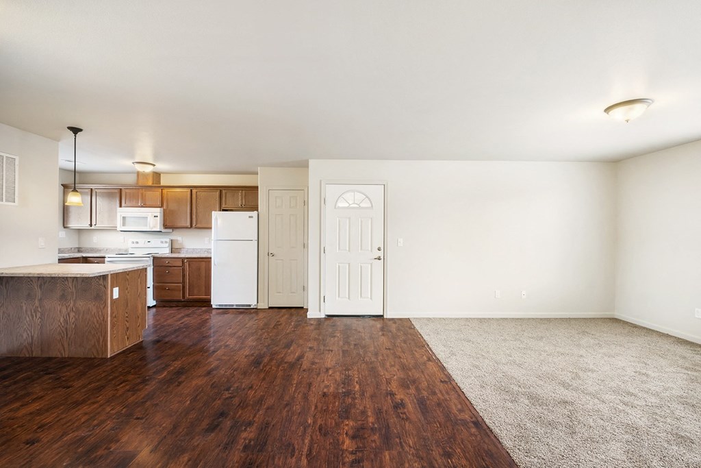 a kitchen and living room with hardwood floors and white walls. Living area carpeted with large window on the right wall. at Pine Tree Park, Kennewick