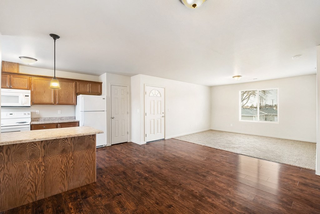 A kitchen with hardwood floors looking into the carpeted living room, with a front door between. A large window is on the right wall. at Pine Tree Park, Kennewick