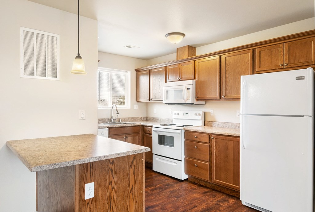 A kitchen with wood cabinets, hardwood floorings, white appliances, and a light-filled window above the sink. at Pine Tree Park, Kennewick, WA