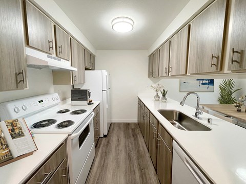 A galley-style kitchen with wood-like flooring, top and bottom cabinet storage, and white appliances. An oven and range, full-size fridge, dishwasher and sink.at The Trail, Snohomish, WA 98290