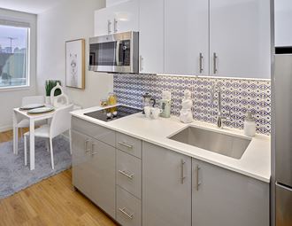 Kitchen with white counters, stainless steel appliances, flat stove top, microwave, and tiled backsplash.
