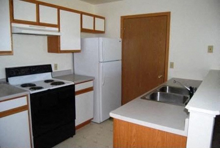 Kitchen with double stainless steel sink, white counters, wood cabinets, full-size fridge, oven, and stovetop.