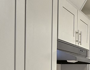 Updated kitchen with stainless steel oven, hood vent, dishwasher and sink from left to right. White countertops and white cabinets. Wood style flooring.